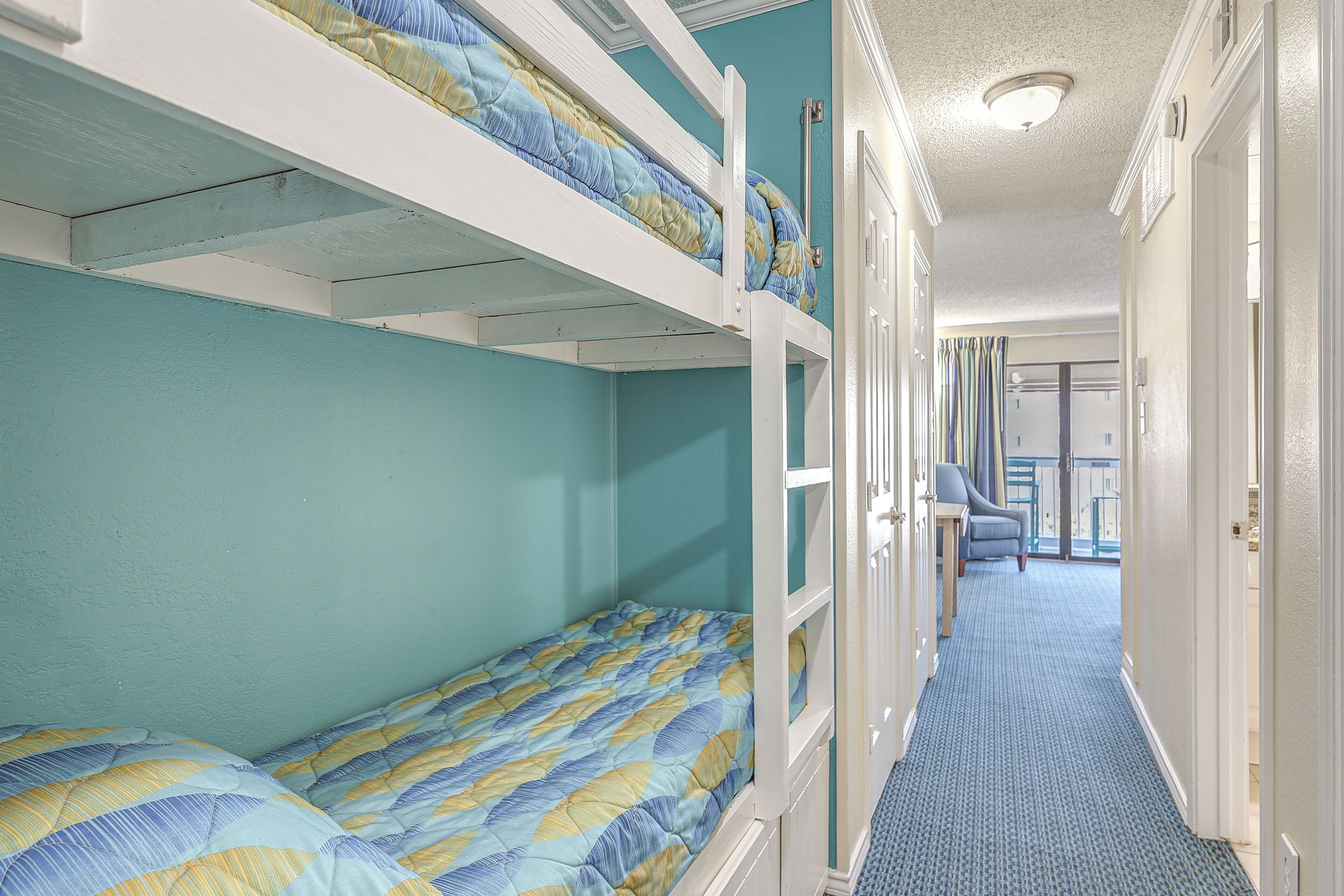 A room with bunk beds, a hallway, and a door leading to a balcony.