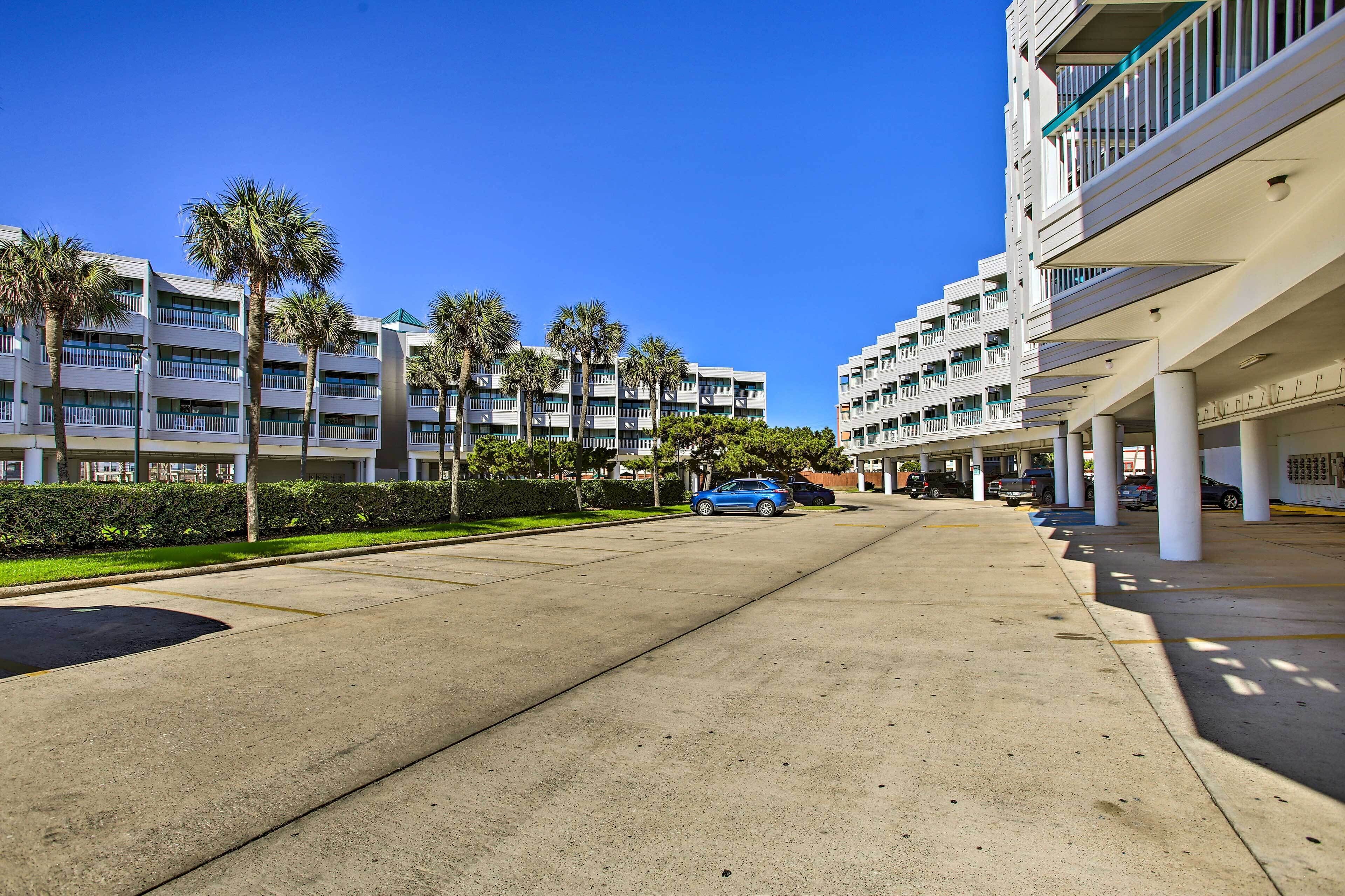 A multi-story hotel with a parking area, palm trees, and a clear blue sky.