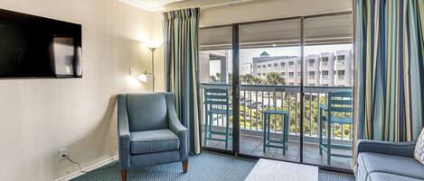 Une chambre d’hôtel avec un canapé, un fauteuil, une table, un téléviseur fixé au mur et un balcon donnant sur des immeubles.
