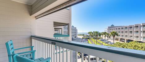 A balcony with teal chairs, a view of a parking lot, and buildings in the background.