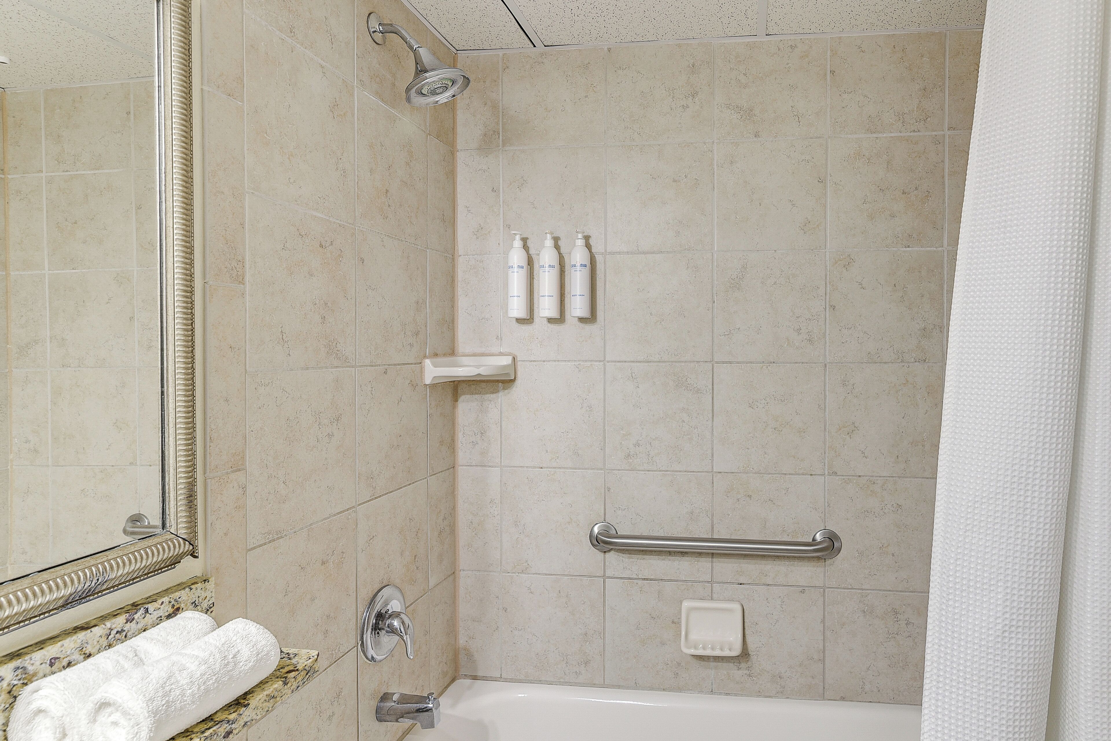 A bathroom with a bathtub, a shower, a handrail, and toiletries on the wall.