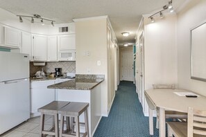 Una cocina con armarios blancos, encimera de granito, cafetera y comedor con mesa y sillas.