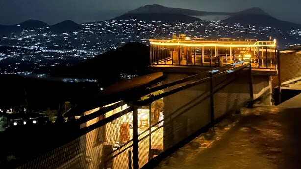 A night view of a building with a glass facade overlooking a cityscape and mountains.
