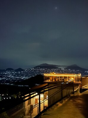 Vue nocturne d’un bâtiment à la façade vitrée, donnant sur un paysage urbain et des montagnes.