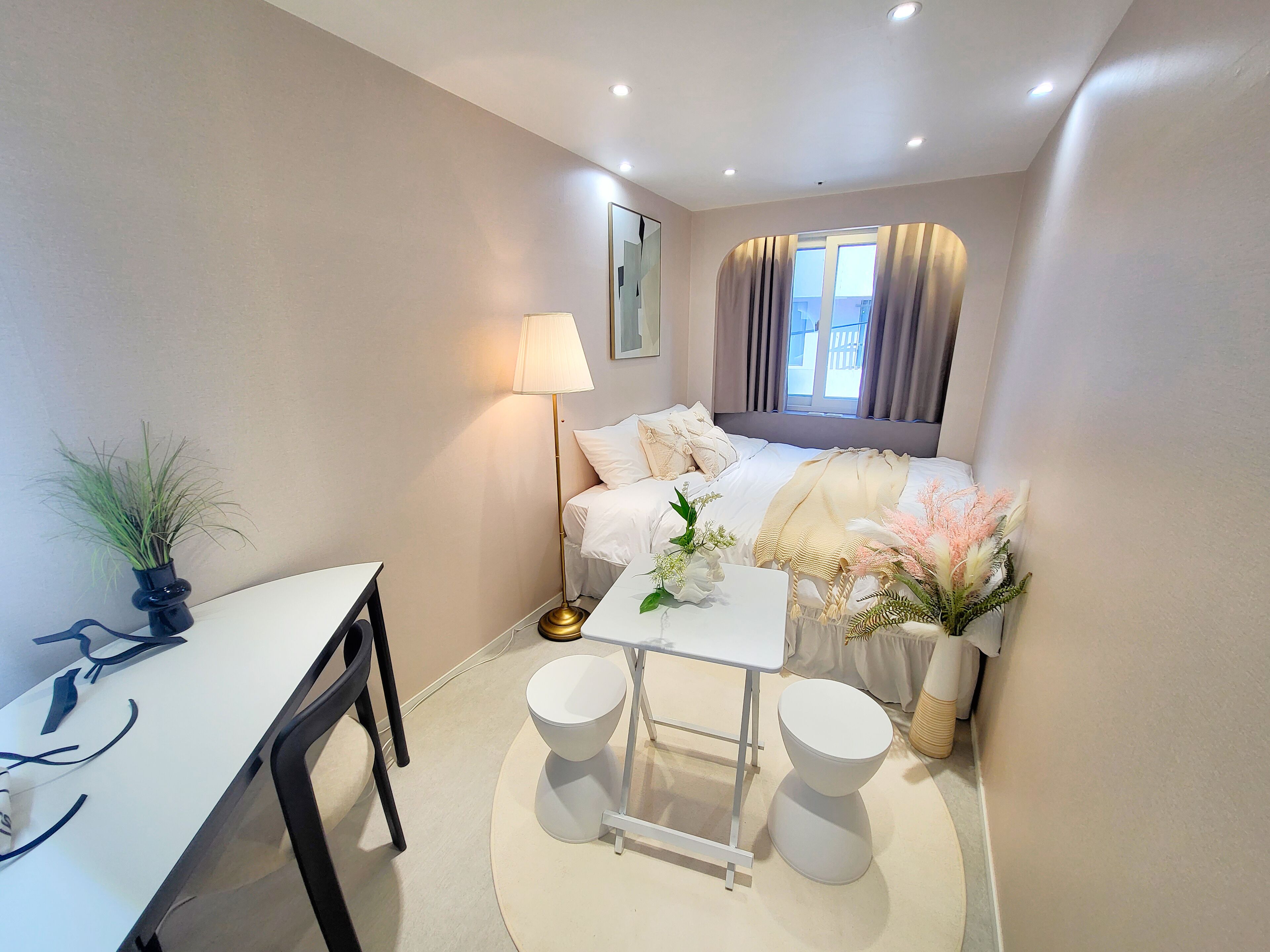 Habitación de hotel pequeña con cama, mesita de noche, lámpara y un escritorio con silla.