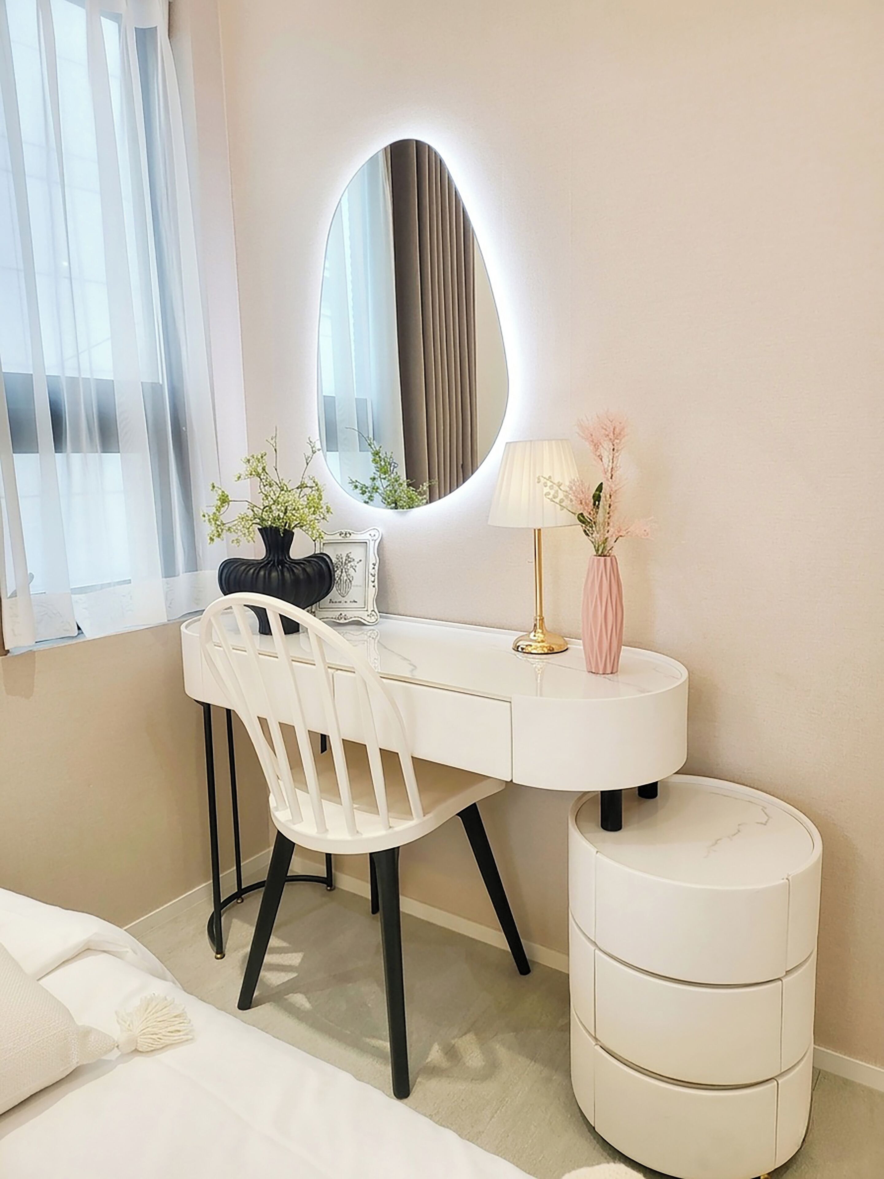 A white desk with a round mirror, a chair, a bedside table, and a bedside lamp.
