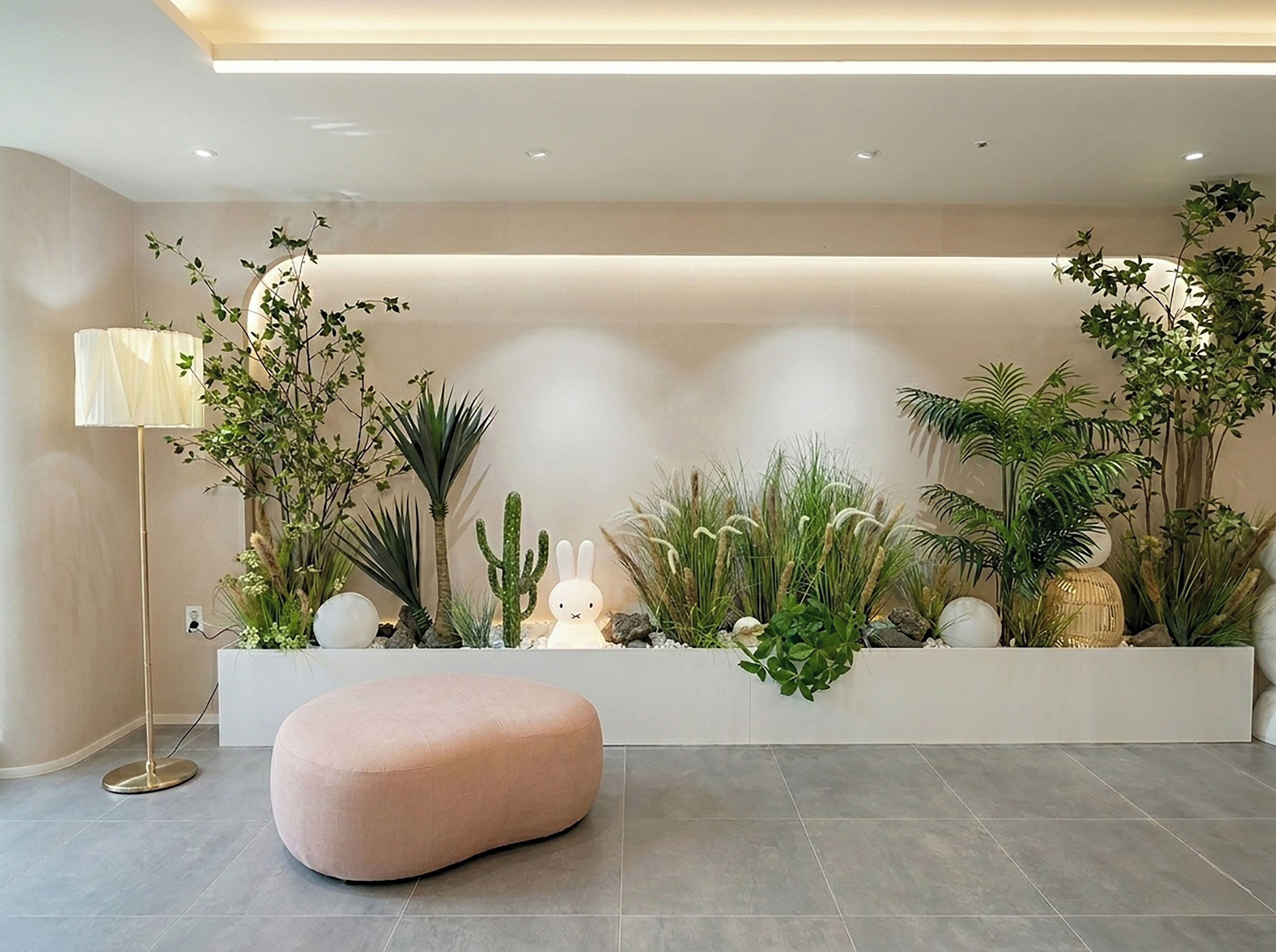A modern interior with a white planter wall, a pink ottoman, and a tall floor lamp.