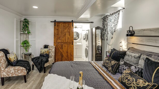 Una camera da letto con un letto, due sedie, una porta in legno e vista su un'area lavanderia.