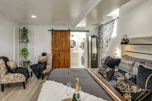 Quarto com cama, duas cadeiras, porta de madeira, espelho e janela com cortinas.