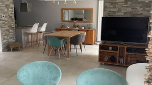 Uma sala de estar moderna com área de jantar, uma televisão de tela plana grande e uma parede de destaque em pedra.