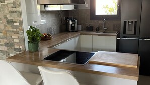 Cozinha moderna com ilha central, dois bancos de barra brancos, máquina de café e uma janela com luz natural.