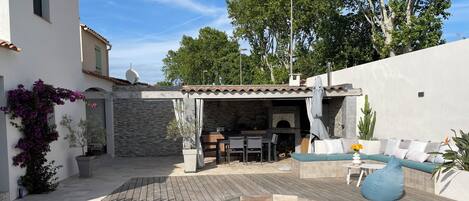 A pool with a wooden deck, a stone wall, and a covered outdoor seating area with a table and chairs.