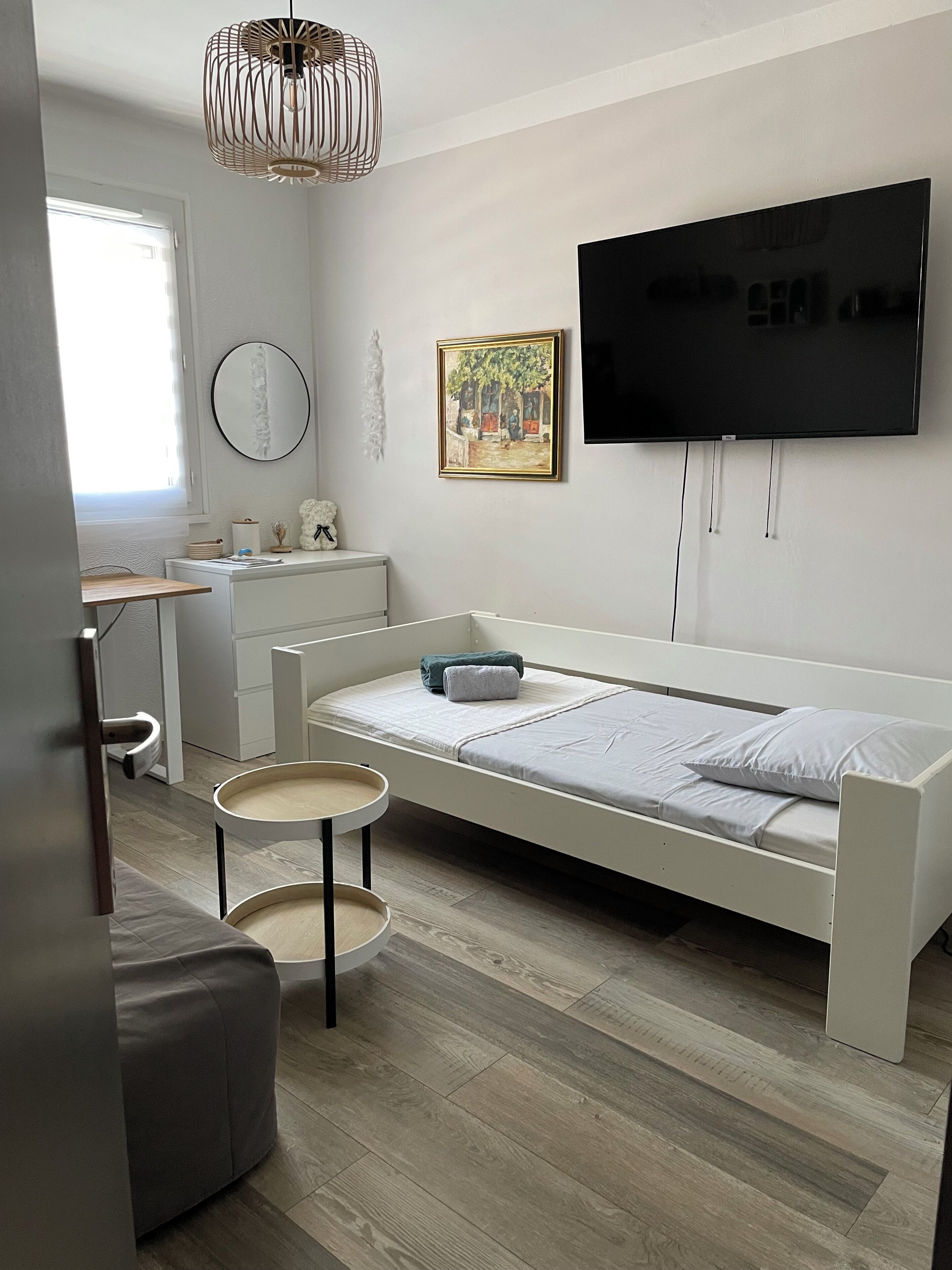 A modern bedroom with a bed, a desk, a chair, a TV, and a painting on the wall.