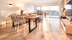 A spacious living area with a large dining table, comfortable seating, a fireplace, and a view of the city.