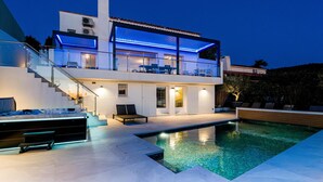 A modern two-story house with a swimming pool, outdoor seating, and a staircase leading to the upper level.