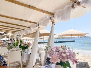 An outdoor seating area with white tables and chairs, arranged under white canopies, overlooking a beach and the sea. - Beautiful villa with airco, pool and hottub (Les Issambres)