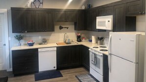 A compact kitchen with dark cabinets, a white refrigerator, a microwave, a dishwasher, and a stove.