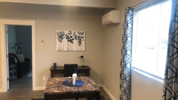 A dining area with a table and chairs, a painting on the wall, and an air conditioning unit.