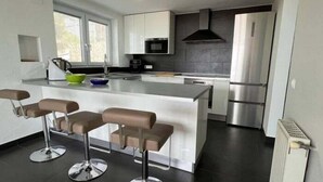 A modern kitchen with a central island, bar stools, stainless steel appliances, and a window providing natural light. - Beautiful house with a swimming pool and views in Roses AV/33 (Roses)