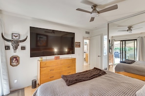 Ein Schlafzimmer mit einem großen Bett, einer Holzkommode, einem Flachbildfernseher und einem Deckenventilator.
