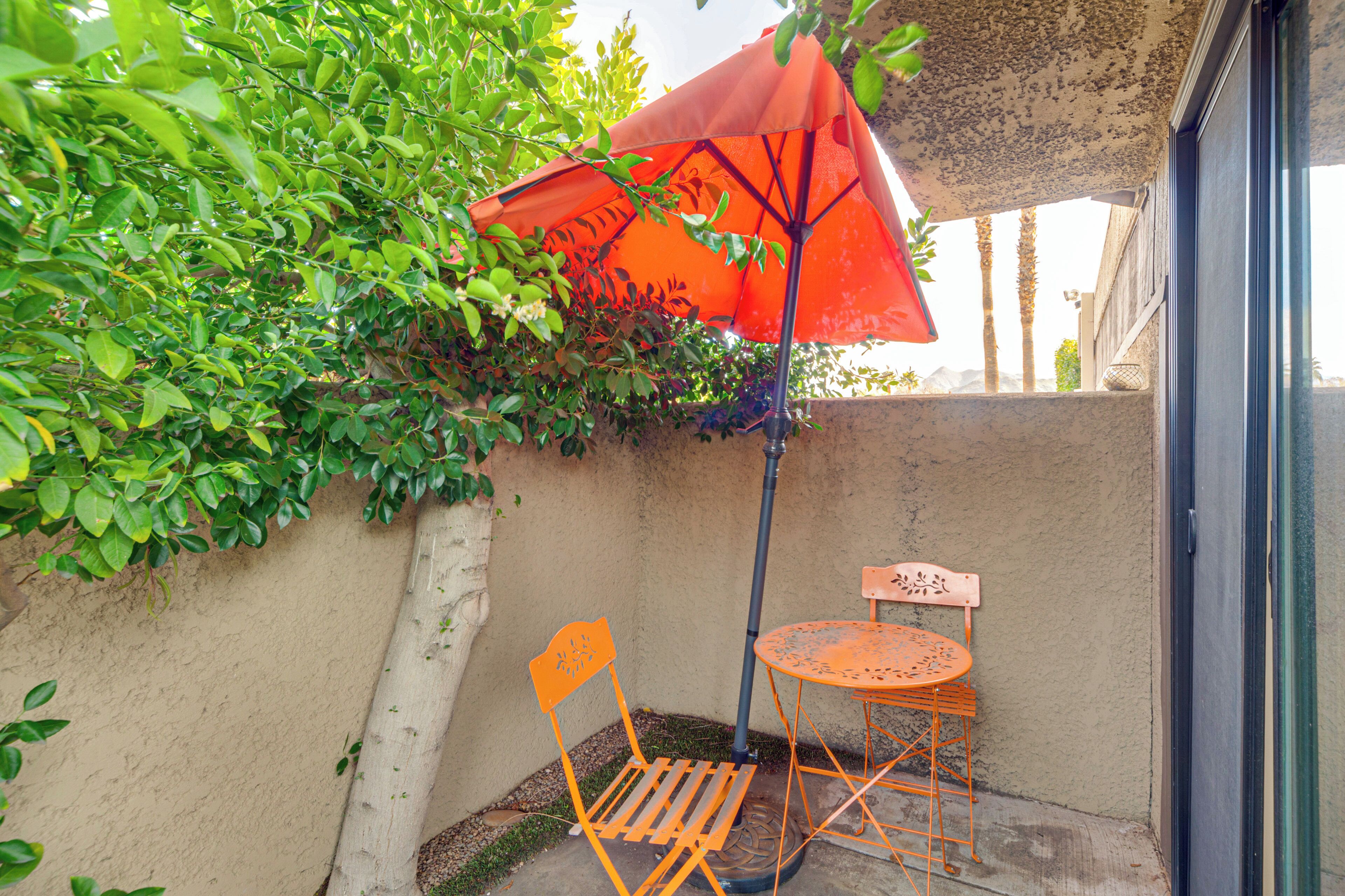 An outdoor seating area with a table and chairs, a red umbrella, and a wall with greenery.