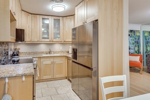 Eine Küche mit Holzschränken, einem Edelstahlkühlschrank, Granitarbeitsplatten und einer gefliesten Spritzschutzwand.