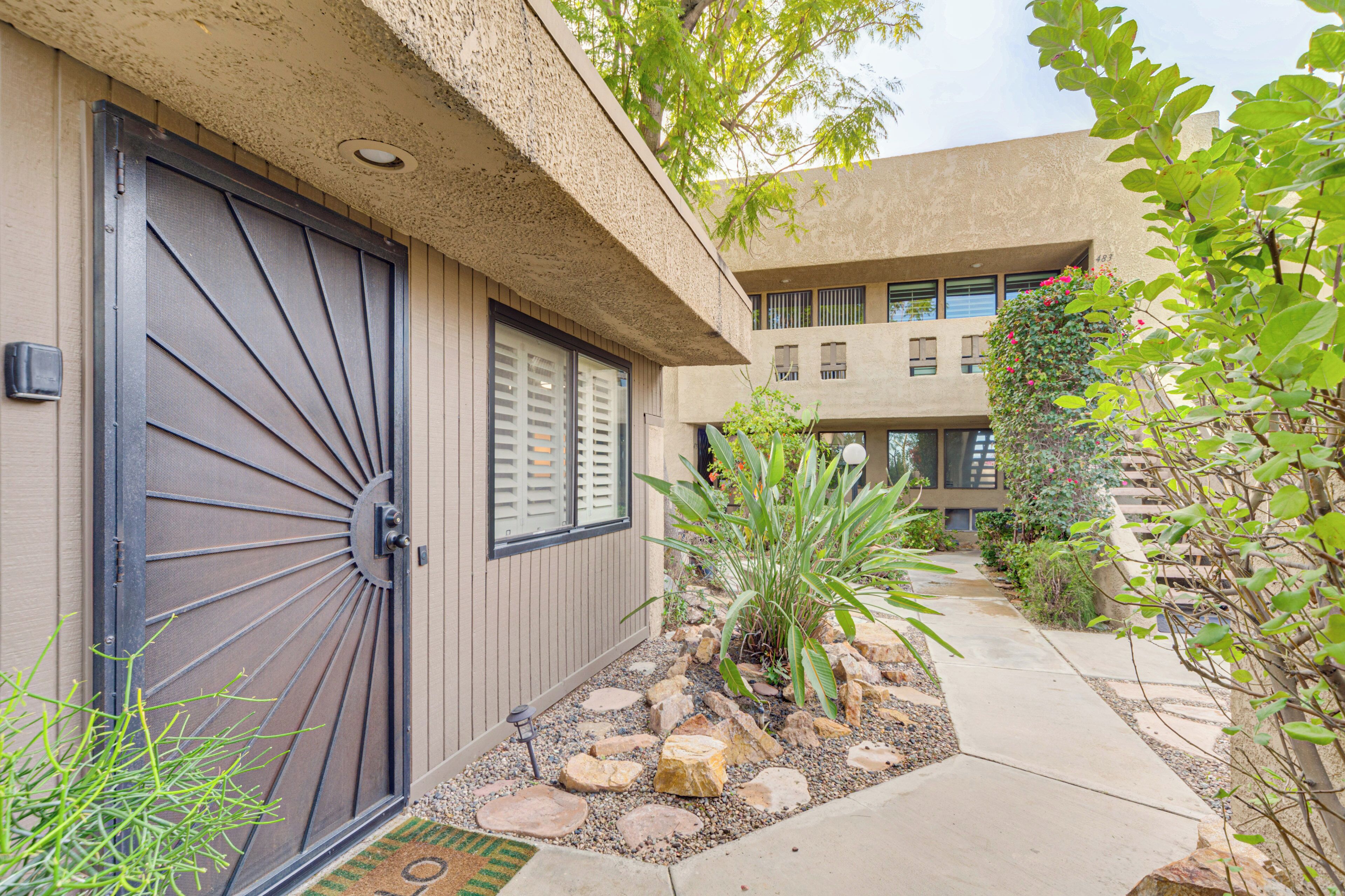 A building with a large metal door, a small garden with rocks and plants, and a pathway leading to the entrance.