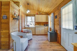 A wooden cabin interior with a dining area, kitchen, and a door with a window.