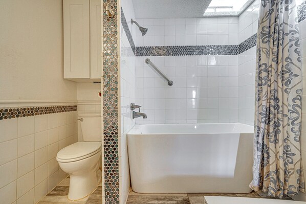 Une salle de bain équipée de toilettes, d’une baignoire, d’une douche et d’une barre d’appui.