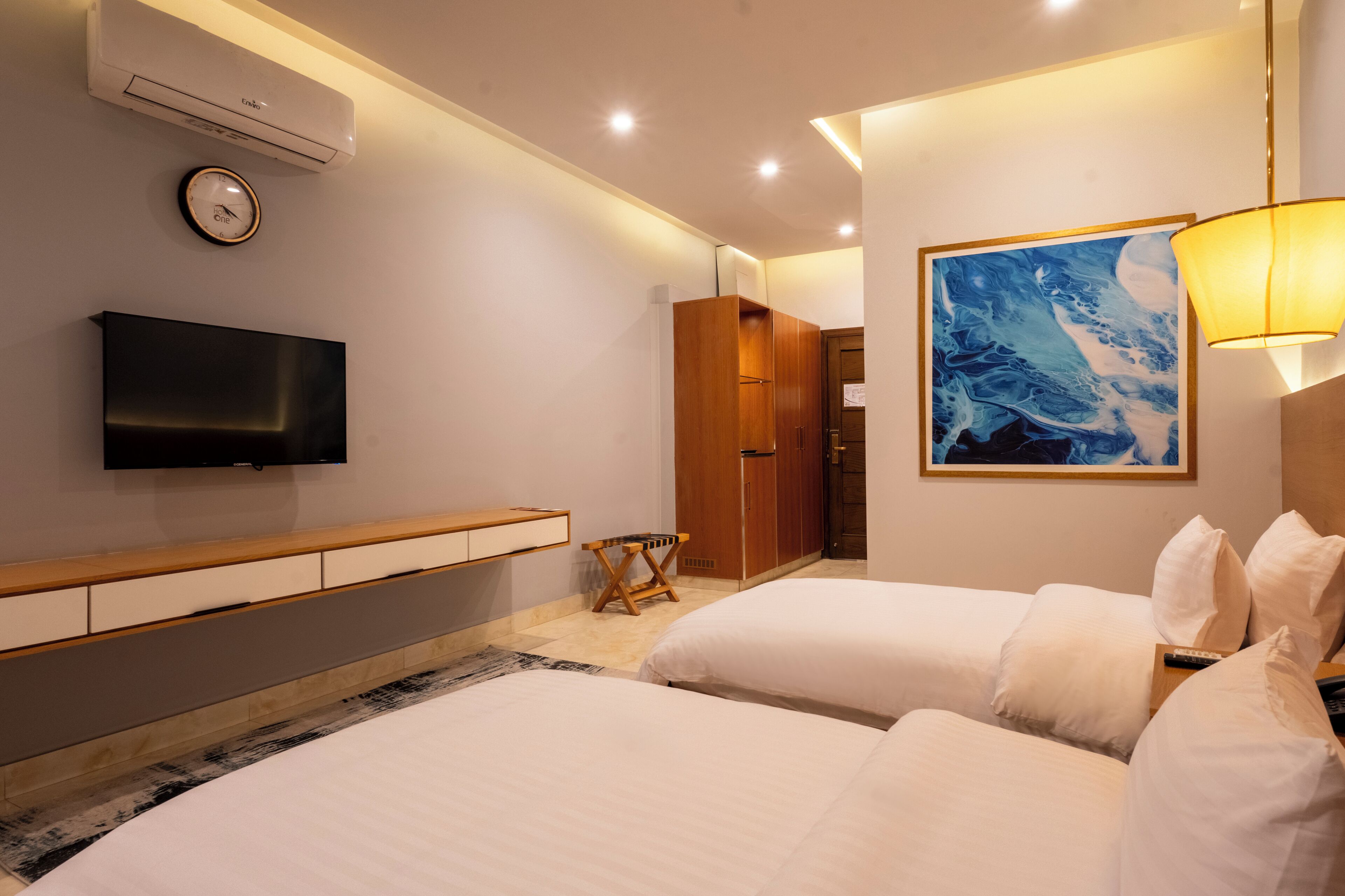 A hotel room with two beds, a TV, a clock, a painting, and a wardrobe.