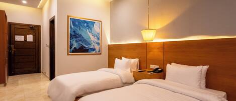 Een hotelkamer met twee bedden, een houten hoofdbord, een schilderij aan de muur, een nachtkastje met een telefoon en een deur met een bericht.