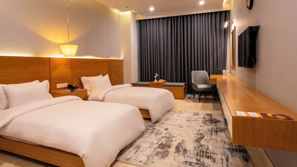 Ein Hotelzimmer mit zwei Betten, einem Schreibtisch, einem Sessel, einem Fernseher und einem großen Fenster mit Vorhängen.
