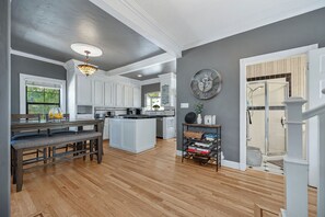 A modern kitchen with white cabinetry, a dining area with a bench, and a hallway leading to a bathroom.