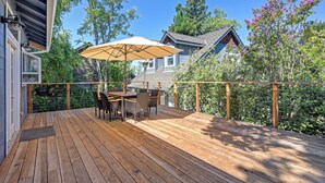 A wooden deck with a table and chairs, surrounded by a wooden railing and a view of a house with a sloped roof. - Remodeled Historic Folsom Craftsman House - Pool - Walk to Sutter St (Folsom)