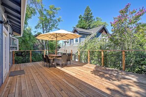 A wooden deck with a table and chairs, surrounded by a wooden railing and a view of a house with a sloped roof. - Remodeled Historic Folsom Craftsman House - Pool - Walk to Sutter St (Folsom)