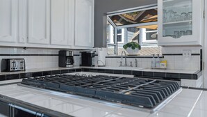 A modern kitchen with a central island, black and white cabinetry, and a window overlooking a residential area. - Remodeled Historic Folsom Craftsman House - Pool - Walk to Sutter St (Folsom)