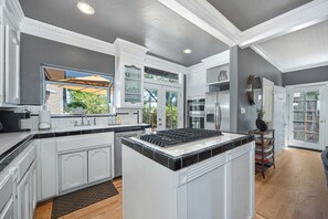 A modern kitchen with white cabinetry, a central island, and a view of the outdoors through a window.