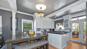 A modern kitchen with a central island, built-in appliances, and a dining area with a bench. - Remodeled Historic Folsom Craftsman House - Pool - Walk to Sutter St (Folsom)