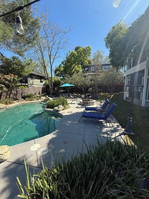 A backyard with a swimming pool, lounge chairs, and a patio area.