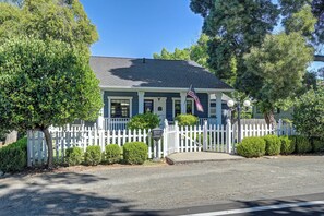 A two-story house with a white picket fence, a front porch, and a flag.