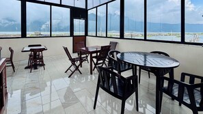 A spacious balcony with a view of mountains and a construction site, furnished with wooden tables and chairs. - Gibico Lakeside Villas Kintamani (Kintamani)