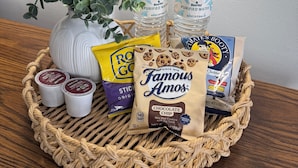 A wicker basket containing a plant, water bottles, a bag of Famous Amos chocolate chip cookies, a bag of Reese's Peanut Butter cups, and a box of Cheddar cheese. - The John Day Motel (John Day)
