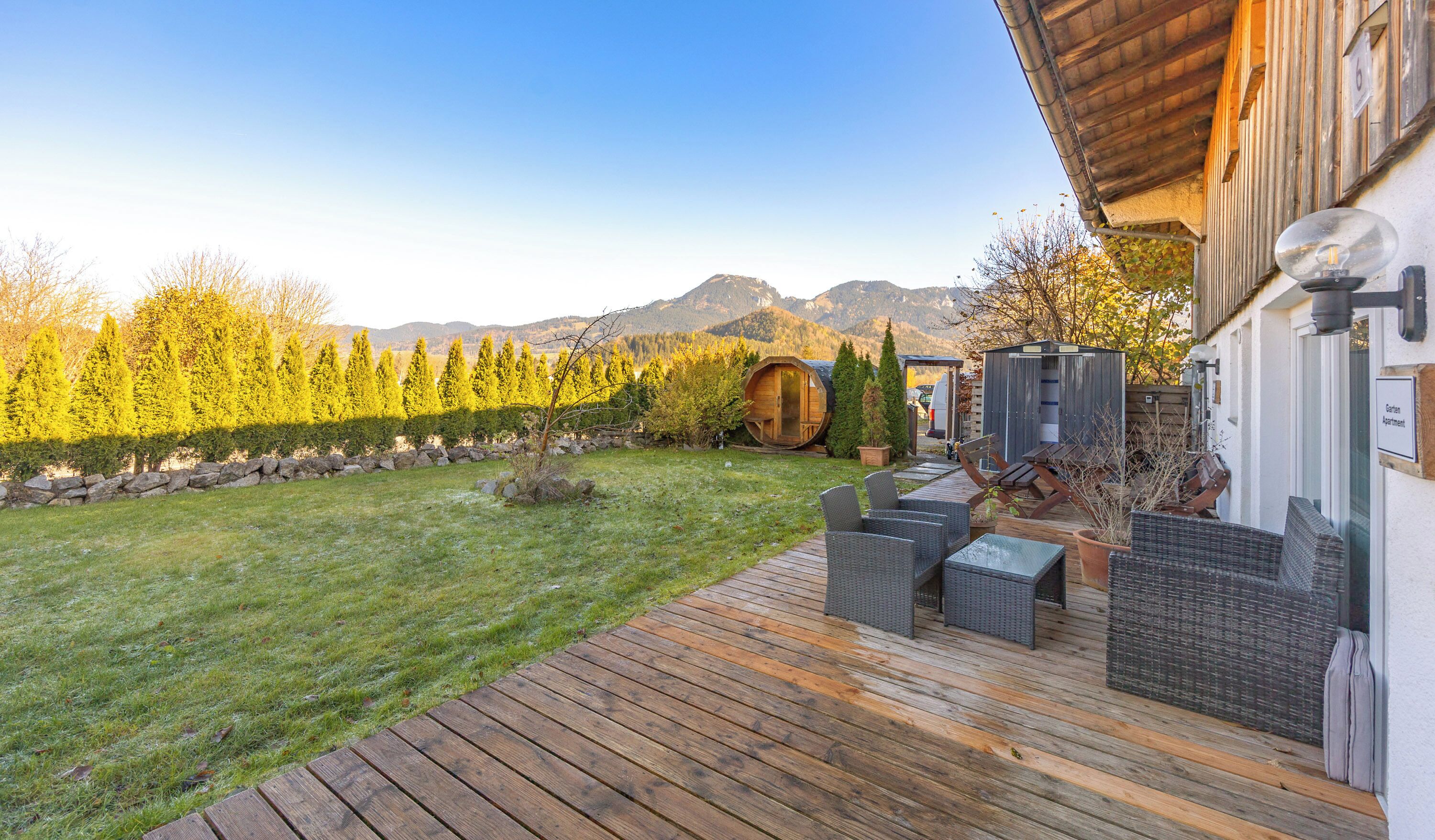 Una terraza de madera con mobiliario exterior, un barril de madera y un cobertizo pequeño.