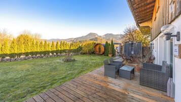 Una terraza de madera con mobiliario exterior, un barril de madera y un cobertizo pequeño.