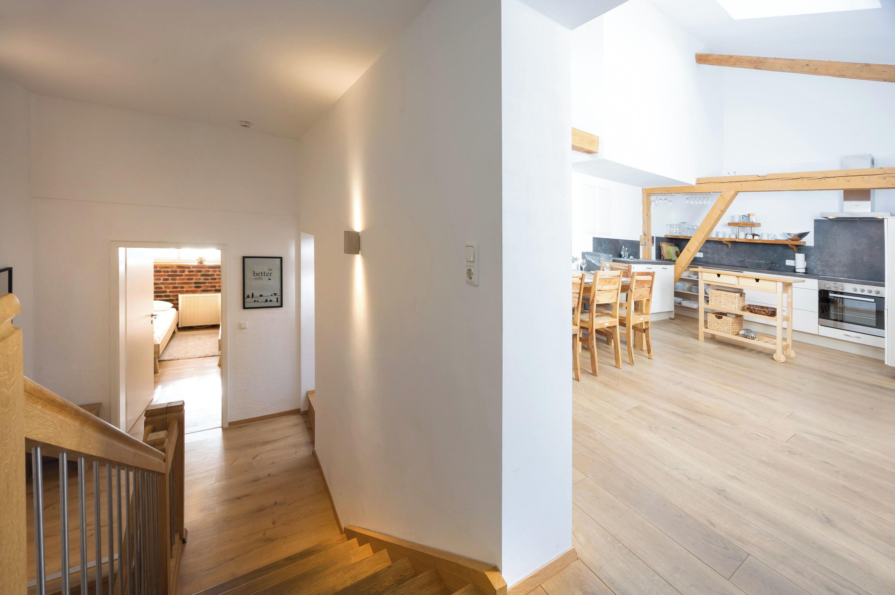 A modern kitchen with wooden flooring, a dining area, and a staircase leading to another room.