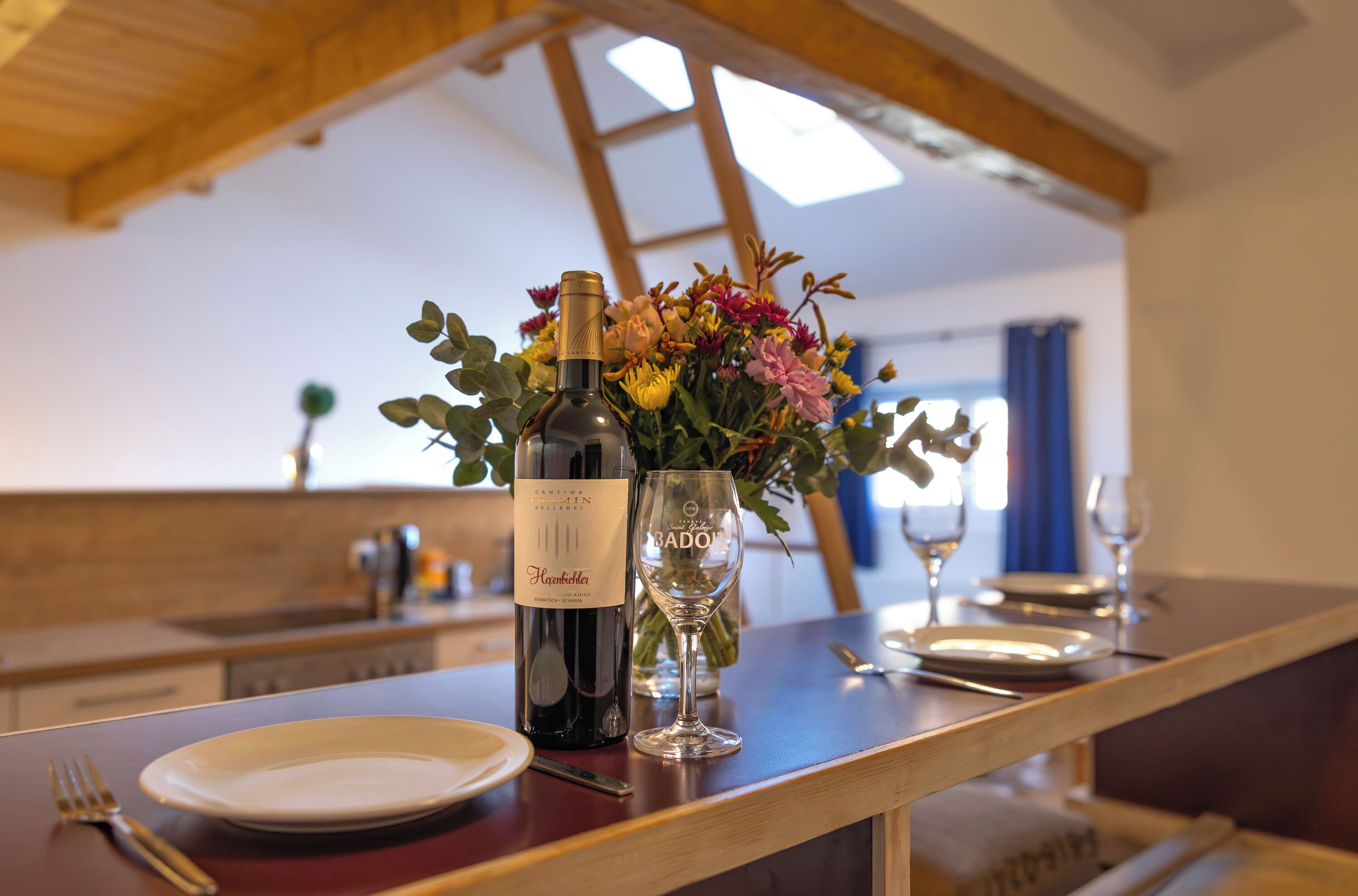 Une table à manger avec une bouteille de vin, un verre et un vase de fleurs.