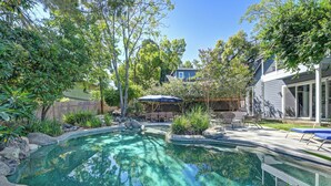 Ein Garten mit Schwimmbad, umgeben von Bäumen und einer Terrassenfläche mit Gartenmöbeln.