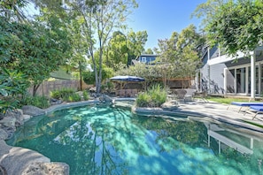 A backyard with a swimming pool, surrounded by trees and a patio area with outdoor furniture.