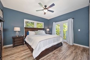 A bedroom with a bed, nightstands, a ceiling fan, and a view through a window.