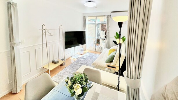 Ett modernt vardagsrum med en platt-TV, ett matbord med en vas med blommor och en soffa med kuddar.